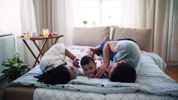 A young affectionate couple cuddling with a little baby indoors on bed. Slow motion.