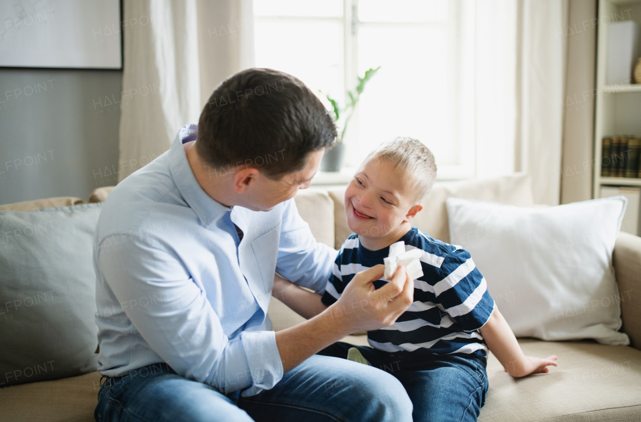 A father with happy down syndrome son indoors at home, talking.