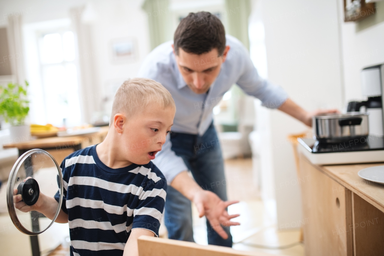 A father with happy down syndrome son indoors in kitchen, cooking.