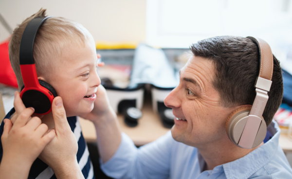 A father with happy down syndrome son indoors at home, using headphones.