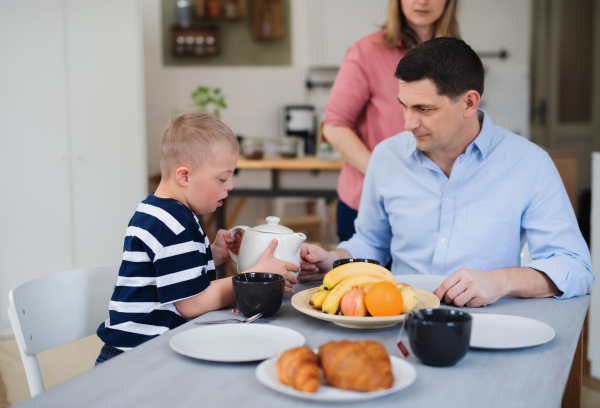 A happy family with down syndrome son at the table, having breakfast.