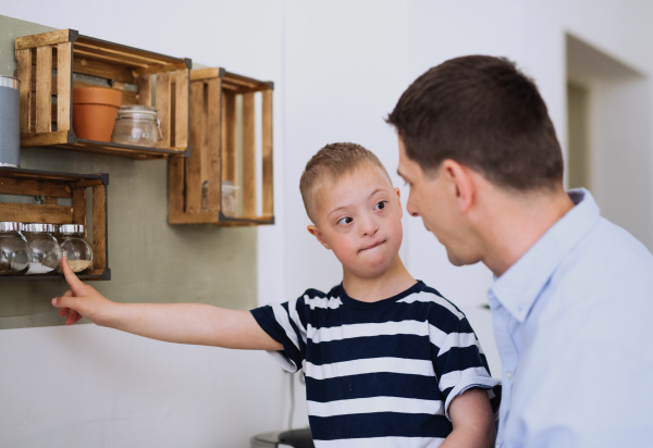 A father with happy down syndrome son indoors in kitchen, cooking.