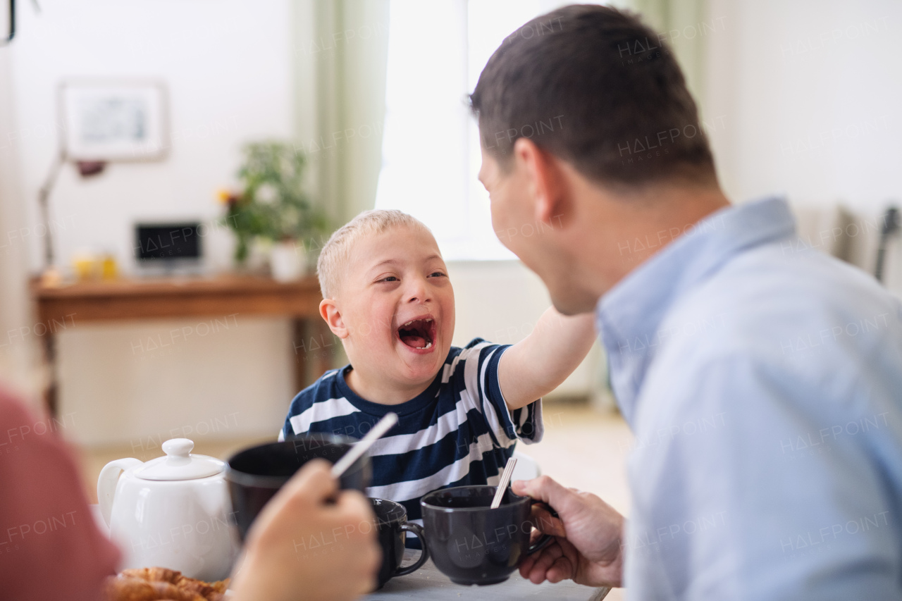 A happy family with down syndrome son at the table, laughing when having breakfast.