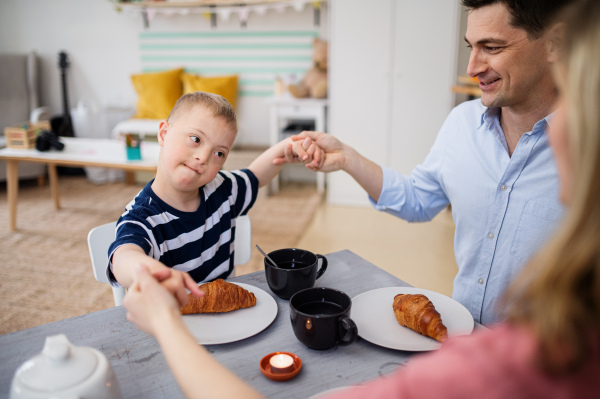 A happy down syndrome boy with parents at the table, praying before breakfast.