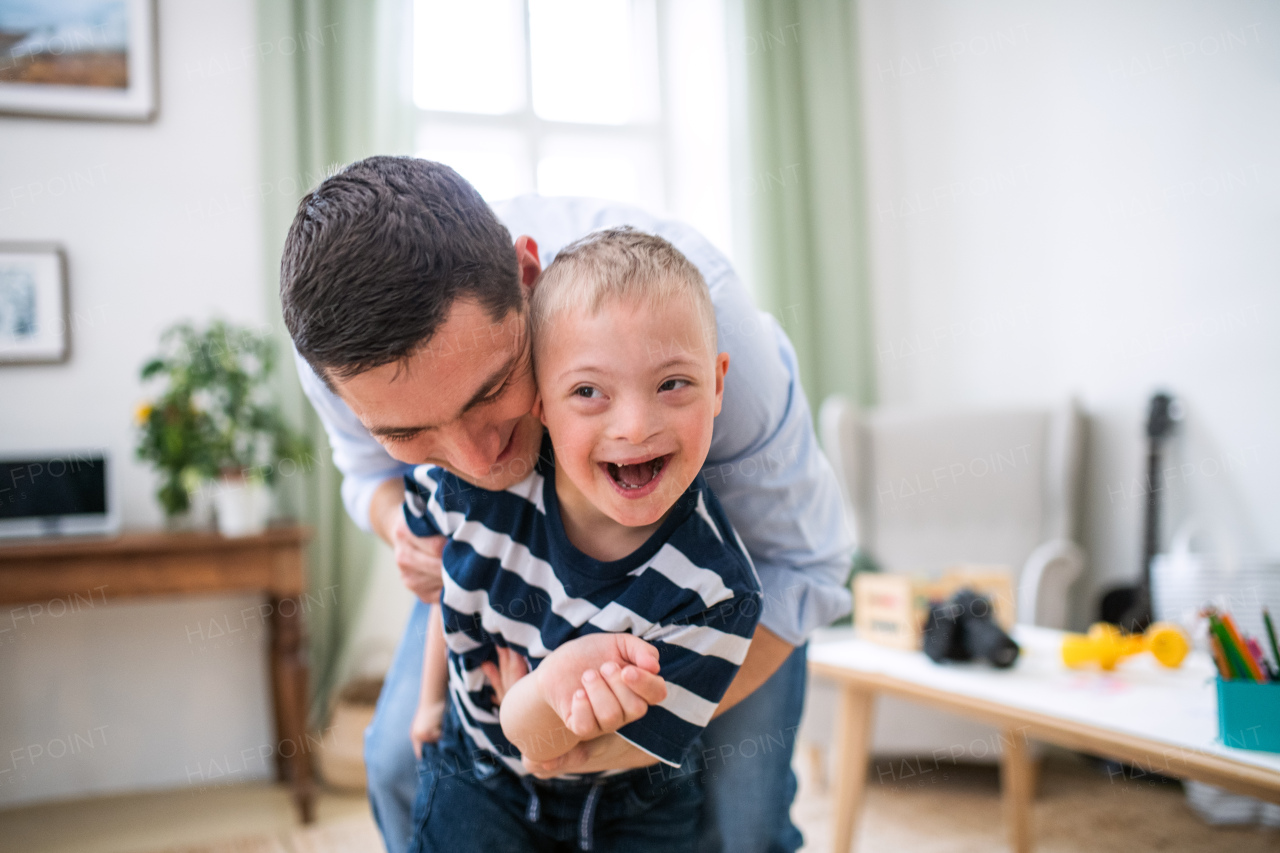 Father with happy down syndrome son indoors at home, having fun laughing.