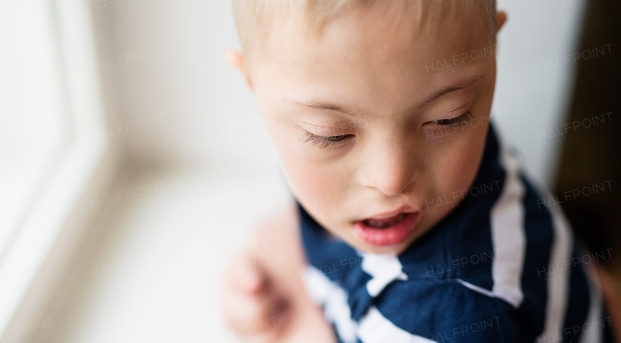 A close-up portrait of down syndrome boy indoors at home. Copy space.