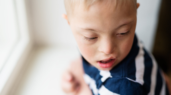 A close-up portrait of down syndrome boy indoors at home. Copy space.