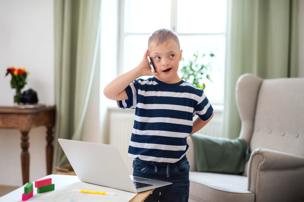 Portrait of happy down syndrome son indoors at home, using smartphone.