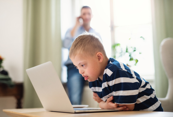 A down syndrome boy with unrecognizable father indoors at home, using laptop.