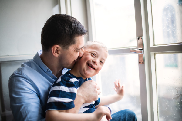 Mature father with happy down syndrome son indoors at home, kissing his cheek.