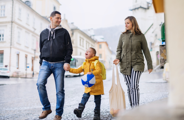 A happy family with down syndrome son walking outdoors, carrying shopping.