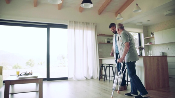 Health visitor and a senior man with crutches during home visit, talking when walking. Slow motion.