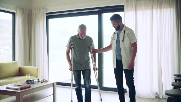 Health visitor and a senior man with crutches during home visit, talking when walking. Slow motion.