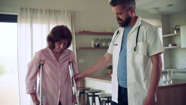 Health visitor and a senior woman with crutches during home visit, walking. Slow motion.