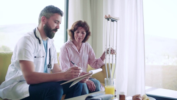 Health visitor and a senior woman with crutches during home visit, talking. Slow motion.