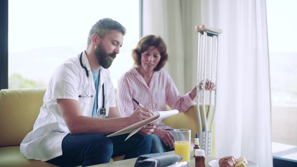 Health visitor and a senior woman with crutches during home visit, talking. Slow motion.