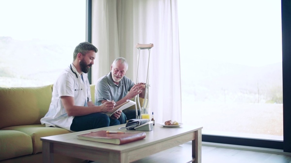 Health visitor and a senior man with crutches during home visit, talking about taking medication. Slow motion.