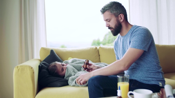 A mature father giving medication to his sick small daughter indoors at home.