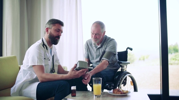 Health visitor and a senior man in wheelchair during home visit, checking blood pressure. Slow motion.