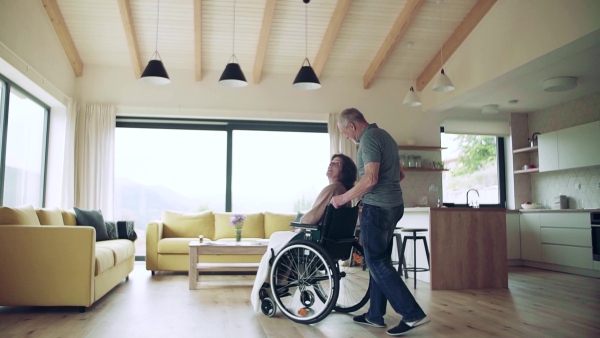 A senior man looking after wife in wheelchair at home, talking. Slow motion.