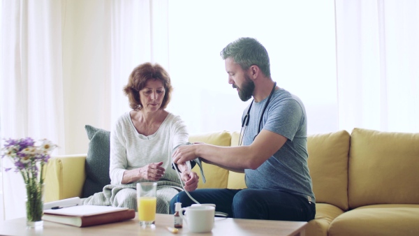 Health visitor and a senior woman during home visit, checking blood pressure.