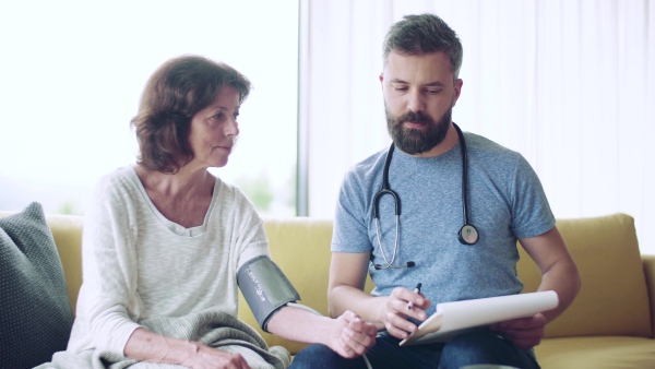 Health visitor and a senior woman during home visit, checking blood pressure.