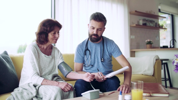 Health visitor and a senior woman during home visit, checking blood pressure.