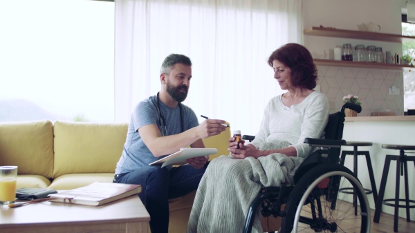 Health visitor and a senior woman in wheelchair during home visit, talking about taking medication.