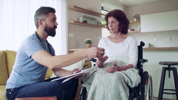 Health visitor and a senior woman in wheelchair during home visit, talking about taking medication.