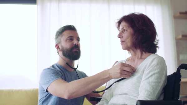 Health visitor examining a senior woman during home visit with stethoscope.