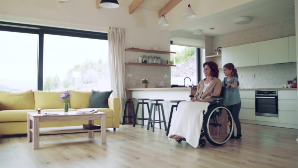 A small girl and her senior grandmother in wheelchair indoors at home.