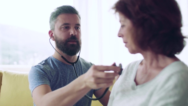 Health visitor examining a senior woman during home visit with stethoscope.