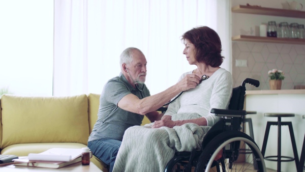 Health visitor examining a senior woman in wheelchair with stethoscope during home visit.