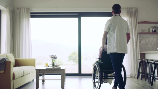 Health visitor and a disabled senior woman in wheelchair during home visit.