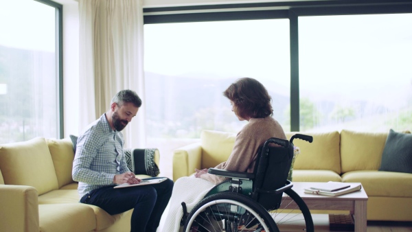 Health visitor and a disabled senior woman in wheelchair during home visit.