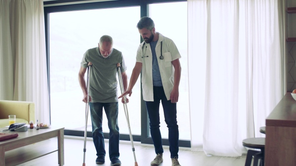 Health visitor and a senior man with crutches during home visit, talking when walking.