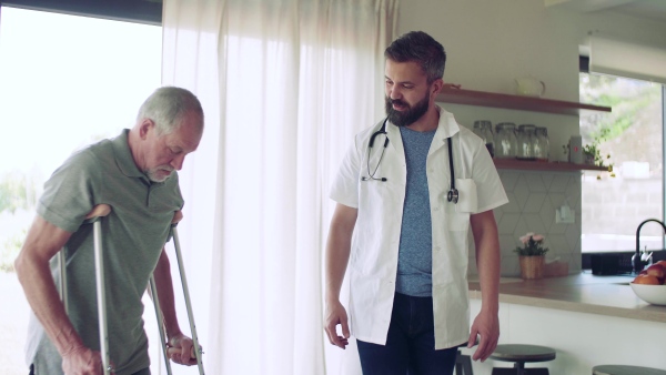 Health visitor and a senior man with crutches during home visit, talking when walking.