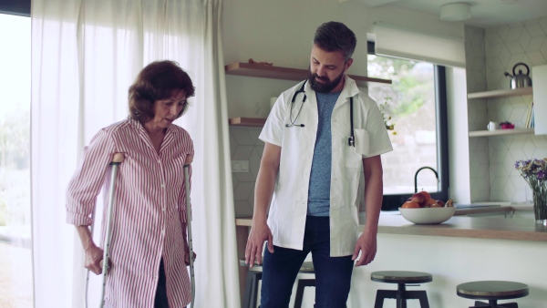 A health visitor and a senior woman with crutches during home visit, walking.