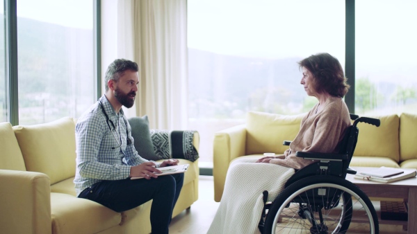 Health visitor and a senior woman in wheelchair during home visit, talking.