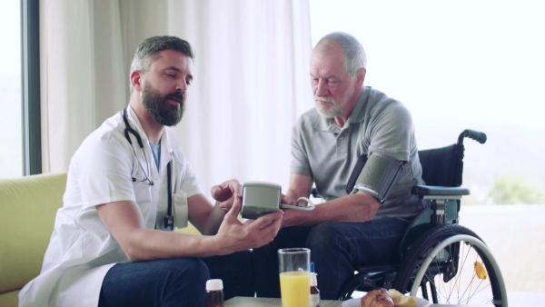 Health visitor and a senior man in wheelchair during home visit, checking blood pressure.