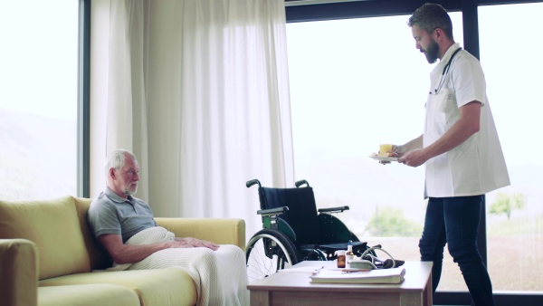 Health visitor bringing snack to a senior man in wheelchair during home visit.