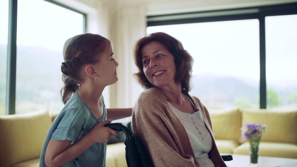 A small girl and her senior grandmother in wheelchair indoors at home. Slow motion.