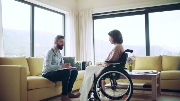 Health visitor and a senior woman in wheelchair during home visit, talking. Slow motion.