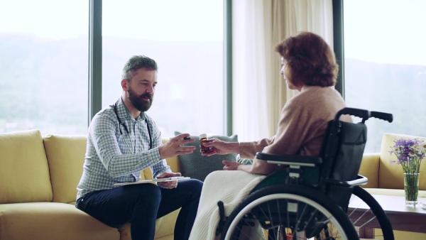 Health visitor and a senior woman in wheelchair during home visit, talking about taking medication. Slow motion.