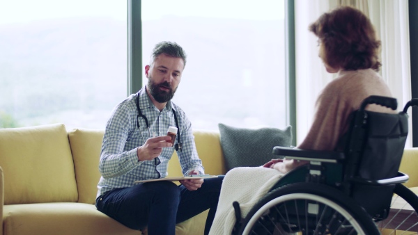 Health visitor and a senior woman in wheelchair during home visit, talking about taking medication.