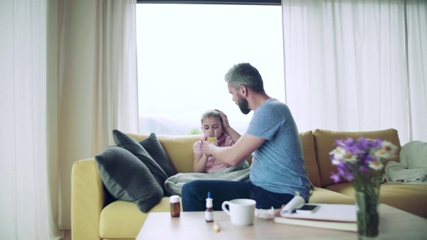 Mature father giving juice to his sick small daughter indoors at home. Slow motion.