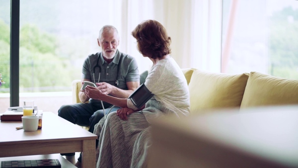 Health visitor and a senior woman during home visit, checking of blood pressure. Slow motion.