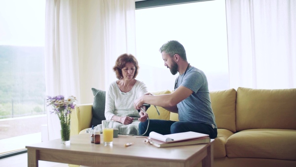 Health visitor and a senior woman during home visit, checking blood pressure. Slow motion.