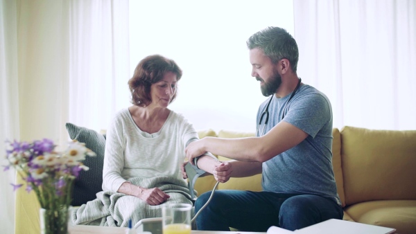 Health visitor and a senior woman during home visit, checking blood pressure. Slow motion.