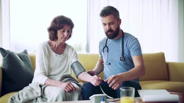 Health visitor and a senior woman during home visit, checking blood pressure. Slow motion.